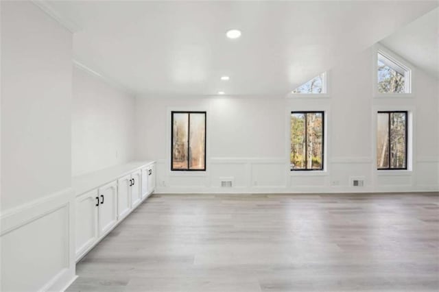 empty room featuring visible vents, vaulted ceiling, and light wood finished floors