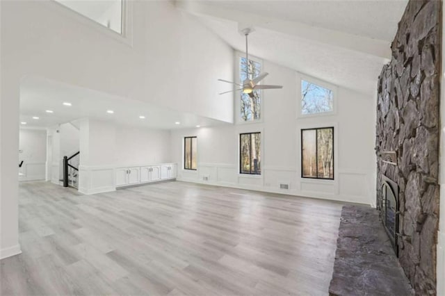 unfurnished living room with a ceiling fan, a decorative wall, a fireplace, light wood finished floors, and lofted ceiling