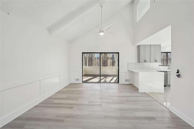 unfurnished dining area with light wood-type flooring, beamed ceiling, high vaulted ceiling, a decorative wall, and ceiling fan