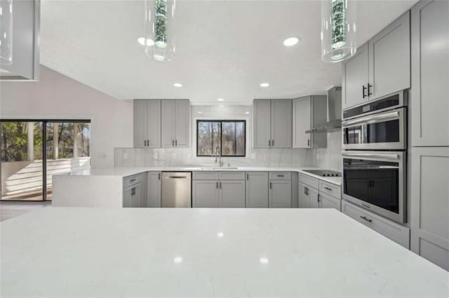 kitchen with gray cabinetry, stainless steel appliances, wall chimney range hood, and a sink