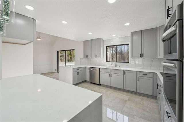 kitchen featuring a peninsula, gray cabinets, a sink, stainless steel appliances, and tasteful backsplash