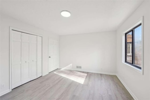 unfurnished bedroom with a closet, visible vents, baseboards, and wood finished floors