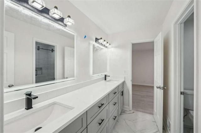 bathroom featuring a sink, marble finish floor, a shower stall, and double vanity