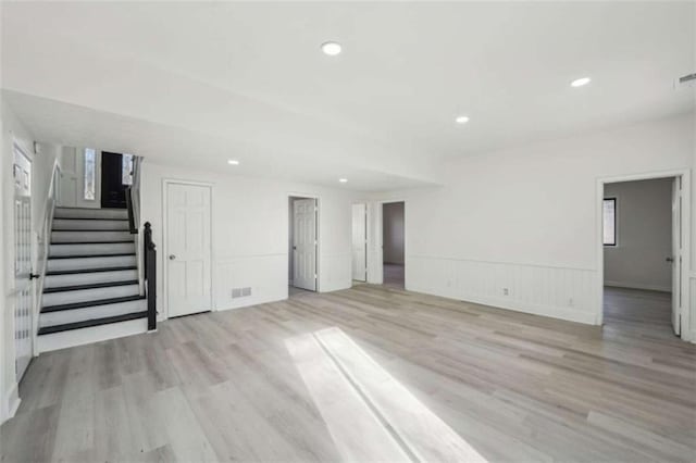 unfurnished living room featuring stairway, visible vents, a wainscoted wall, recessed lighting, and light wood-style floors