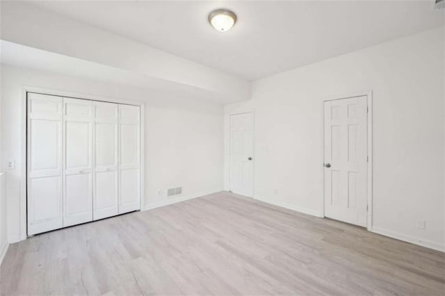 unfurnished bedroom featuring visible vents, baseboards, a closet, and wood finished floors