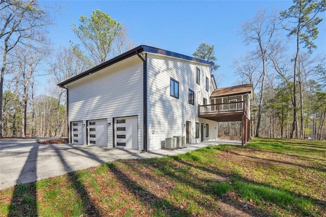 view of property exterior with a deck, driveway, central AC, a yard, and an attached garage