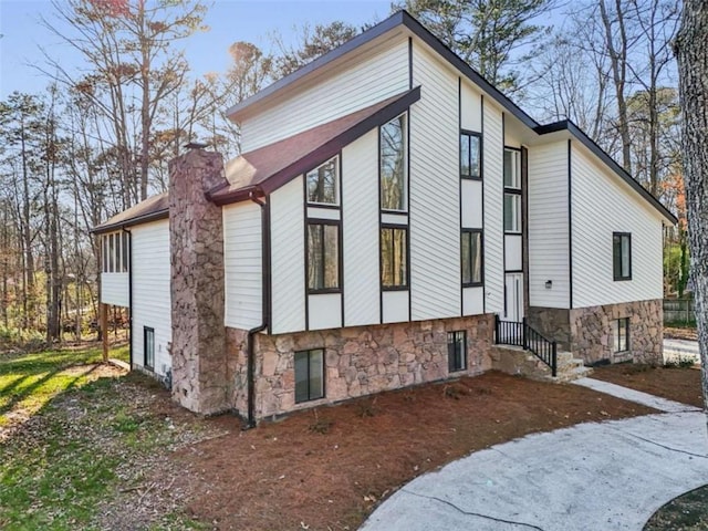 view of side of home featuring stone siding, entry steps, and a chimney