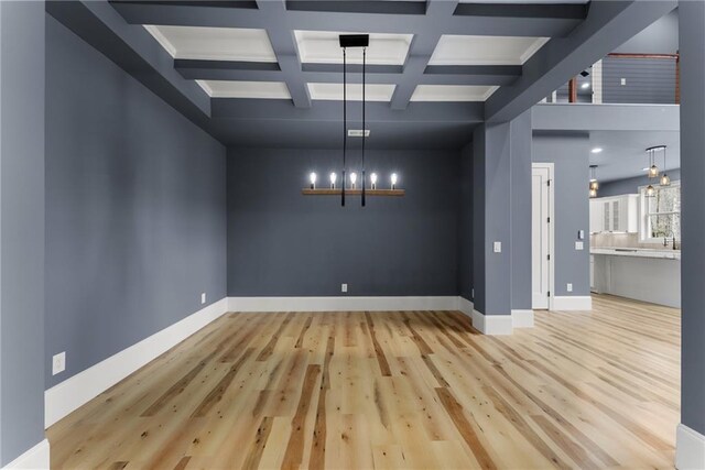 unfurnished dining area with beamed ceiling, coffered ceiling, a chandelier, and light hardwood / wood-style flooring