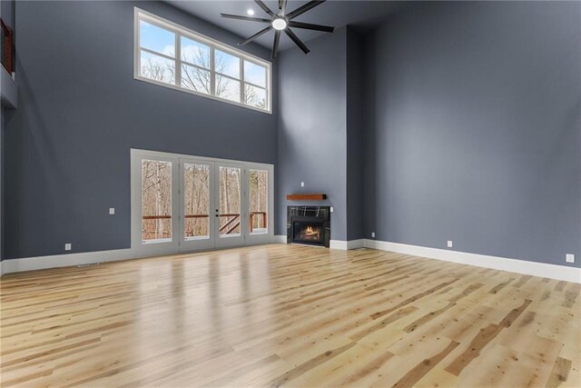 unfurnished living room featuring a towering ceiling, ceiling fan, and light hardwood / wood-style flooring