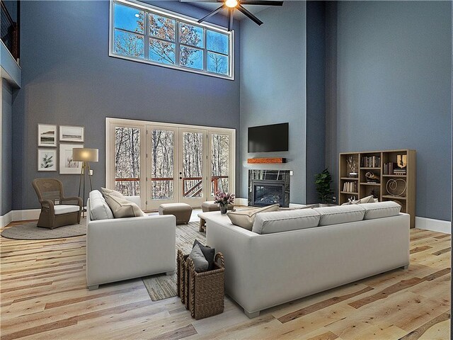 living room featuring ceiling fan, french doors, a high ceiling, and light wood-type flooring