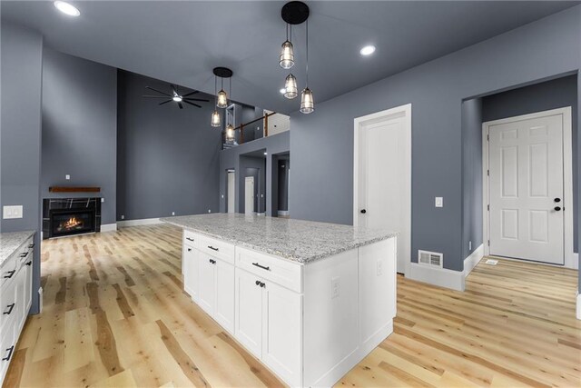 kitchen with light stone countertops, a center island, pendant lighting, and white cabinets