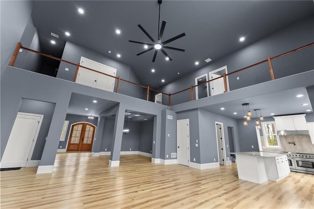 living area with baseboards, a towering ceiling, french doors, light wood-style floors, and recessed lighting