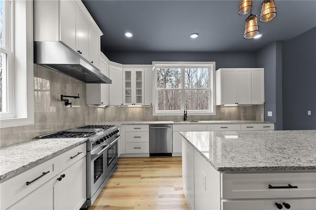 kitchen with decorative light fixtures, stainless steel appliances, a sink, white cabinetry, and glass insert cabinets