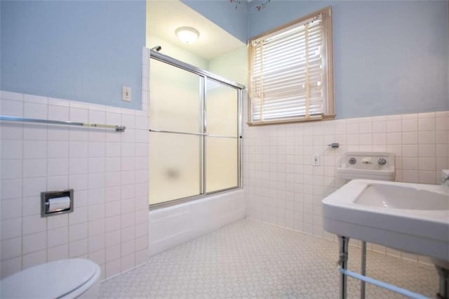 full bathroom featuring combined bath / shower with glass door, sink, tile walls, tile patterned flooring, and toilet