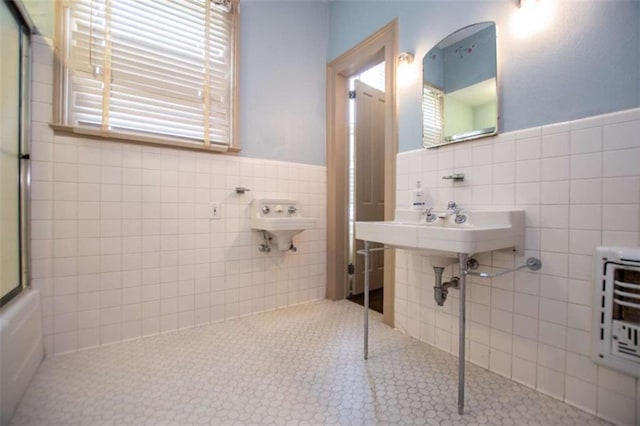 bathroom with heating unit, tile patterned floors, bath / shower combo with glass door, and tile walls