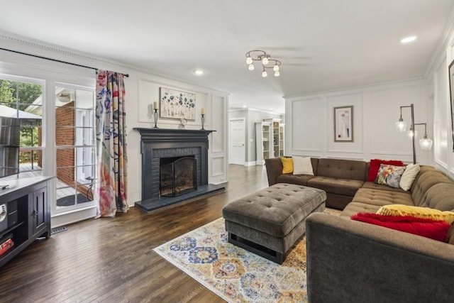 living room featuring a decorative wall, crown molding, a fireplace, dark wood-type flooring, and recessed lighting