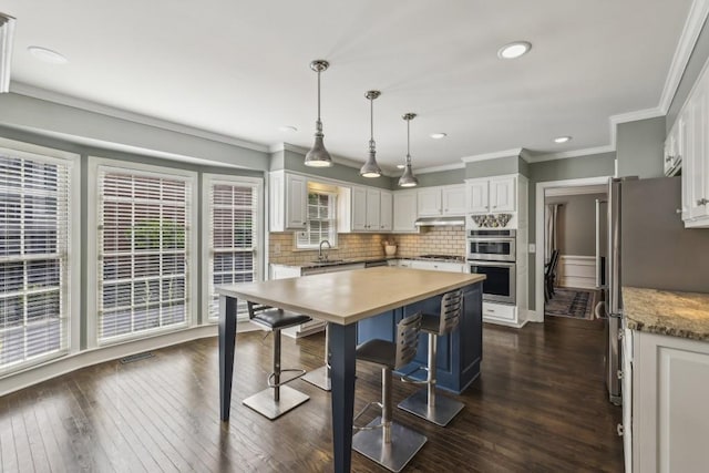 kitchen featuring stainless steel appliances, white cabinetry, under cabinet range hood, a sink, and tasteful backsplash