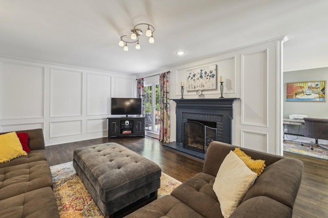 living room with a decorative wall, a fireplace, dark wood-style flooring, ornamental molding, and recessed lighting