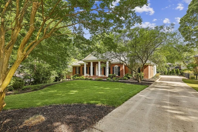 greek revival house featuring concrete driveway, a front yard, and a porch