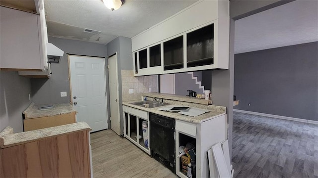 kitchen with sink, white cabinetry, black dishwasher, tasteful backsplash, and light wood-type flooring