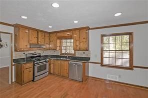 kitchen with brown cabinetry, dark countertops, under cabinet range hood, stainless steel appliances, and recessed lighting