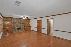 unfurnished living room with built in shelves, ceiling fan, wood finished floors, and visible vents