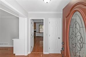 foyer entrance with crown molding, visible vents, and wood finished floors