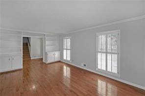 unfurnished living room featuring baseboards, ornamental molding, and wood finished floors