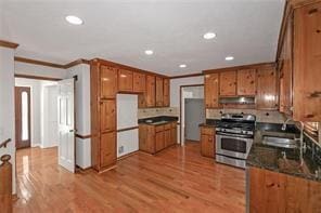 kitchen featuring dark countertops, brown cabinets, gas stove, a sink, and under cabinet range hood