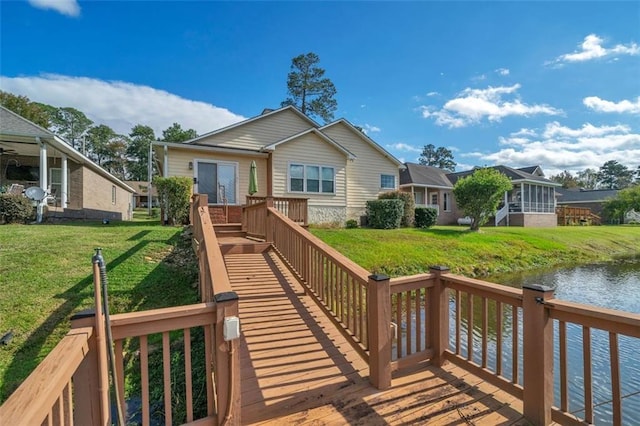 rear view of house with a deck with water view, a lawn, and a sunroom