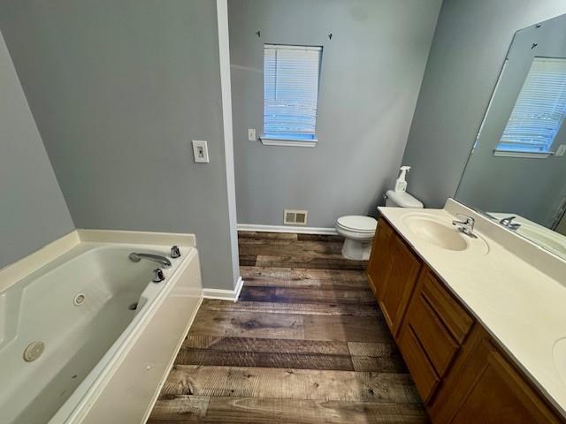 full bath with wood finished floors, a jetted tub, double vanity, toilet, and baseboards
