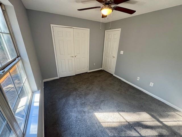 unfurnished bedroom featuring baseboards, dark colored carpet, a closet, and ceiling fan