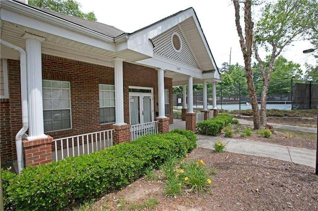 view of home's exterior with brick siding, a porch, and fence