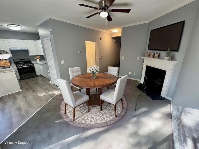 dining space with a ceiling fan, ornamental molding, a fireplace with flush hearth, baseboards, and wood finished floors