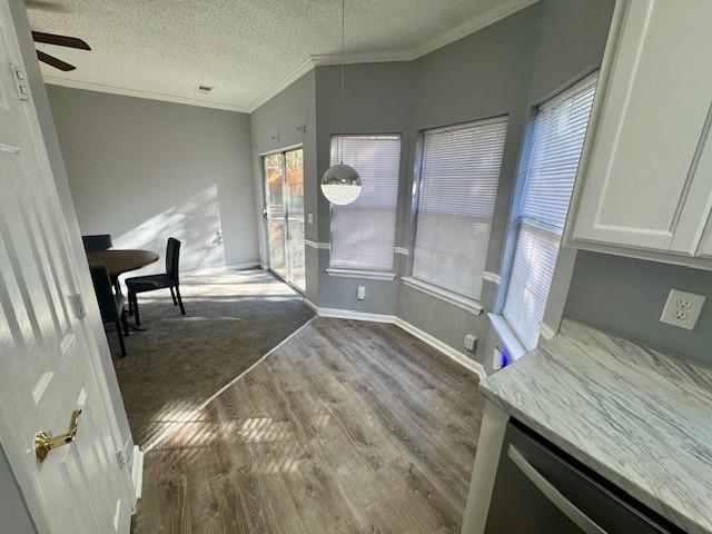 unfurnished dining area featuring wood finished floors, ornamental molding, ceiling fan, a textured ceiling, and baseboards