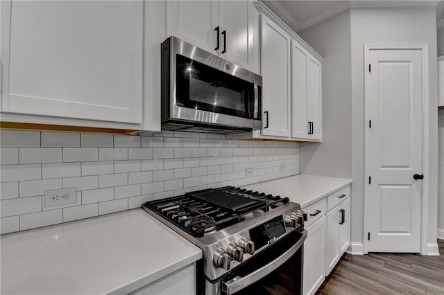 kitchen featuring appliances with stainless steel finishes, light countertops, crown molding, white cabinets, and decorative backsplash