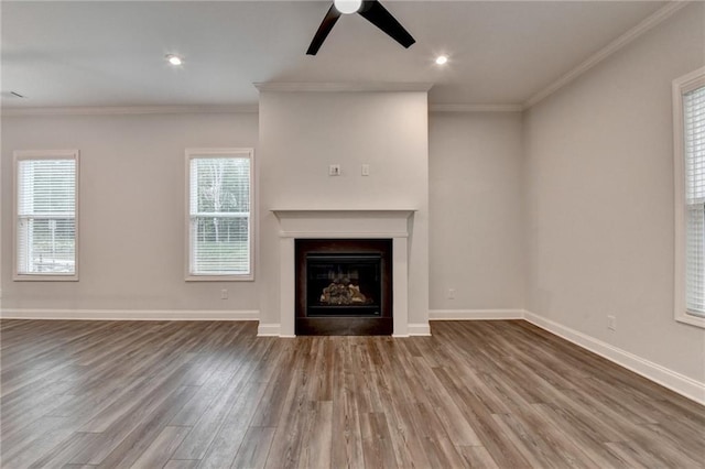 unfurnished living room with a ceiling fan, wood finished floors, crown molding, a fireplace, and baseboards