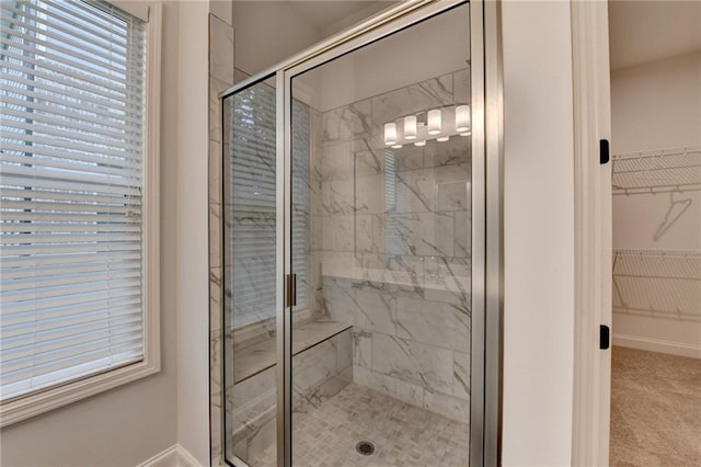 bathroom with a shower stall, a walk in closet, baseboards, and plenty of natural light