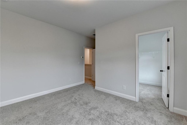 unfurnished bedroom featuring carpet, baseboards, a walk in closet, and a closet