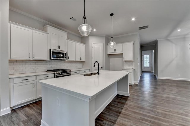 kitchen featuring appliances with stainless steel finishes, a sink, ornamental molding, wood finished floors, and a kitchen island with sink