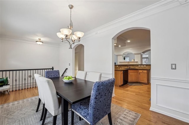 dining area featuring arched walkways, a notable chandelier, light wood-style floors, and ornamental molding