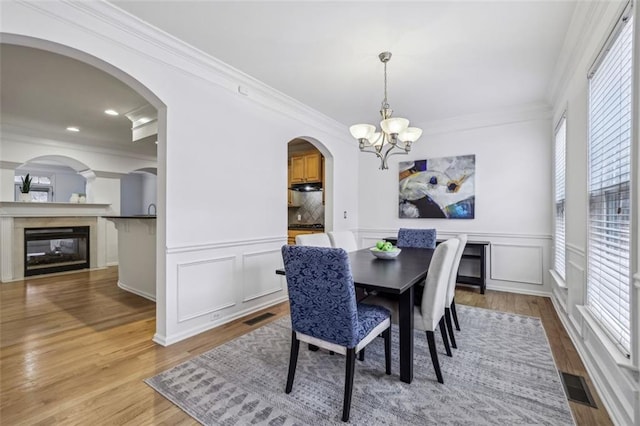 dining area featuring arched walkways, visible vents, a notable chandelier, and wood finished floors