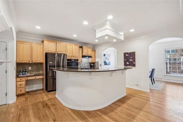 kitchen with a breakfast bar, light brown cabinetry, black fridge with ice dispenser, wall oven, and arched walkways