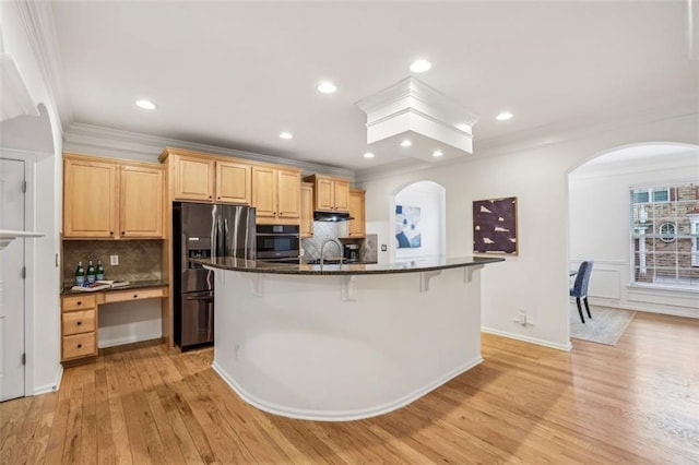 kitchen featuring black refrigerator with ice dispenser, a breakfast bar, arched walkways, wall oven, and light brown cabinets