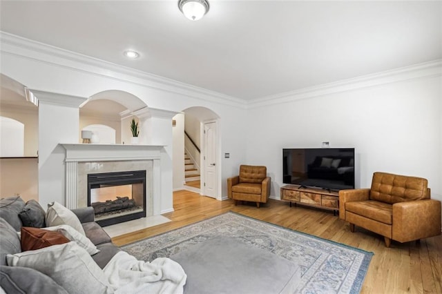 living area with crown molding, stairs, wood finished floors, a tiled fireplace, and arched walkways