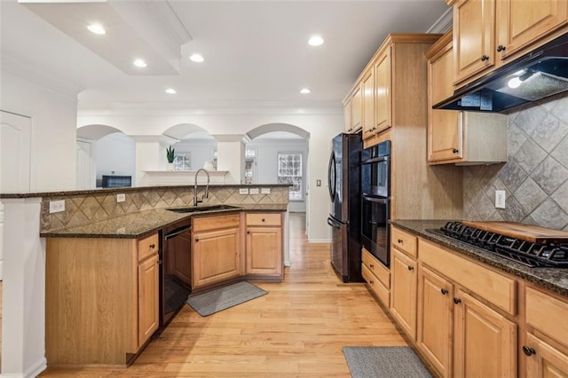 kitchen with under cabinet range hood, dark stone counters, a sink, arched walkways, and black appliances