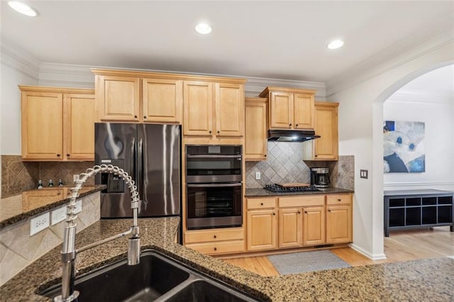 kitchen with under cabinet range hood, dark stone countertops, appliances with stainless steel finishes, and light brown cabinetry