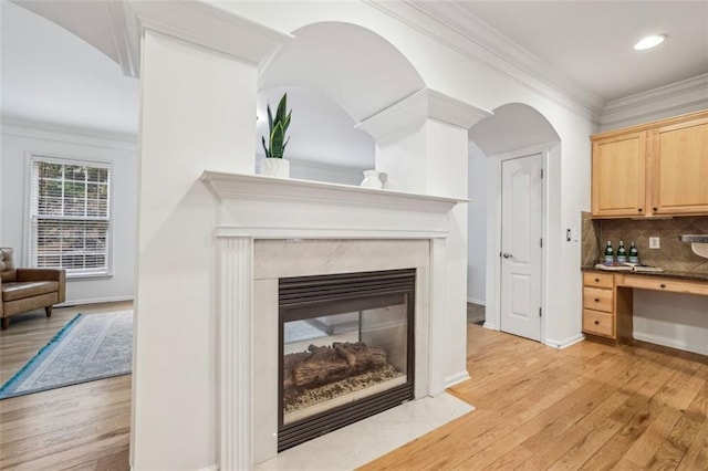 interior space featuring tasteful backsplash, a premium fireplace, crown molding, and wood finished floors