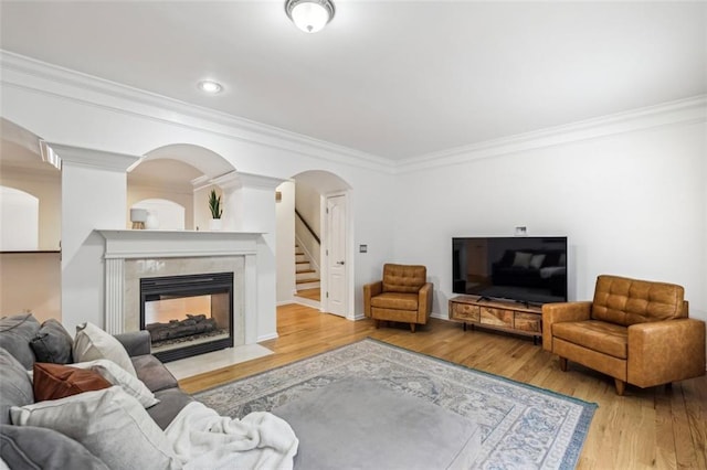 living area featuring stairs, ornamental molding, a fireplace, wood finished floors, and arched walkways