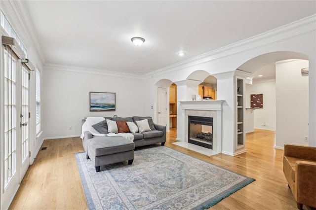 living room featuring arched walkways, a fireplace with flush hearth, crown molding, and light wood finished floors
